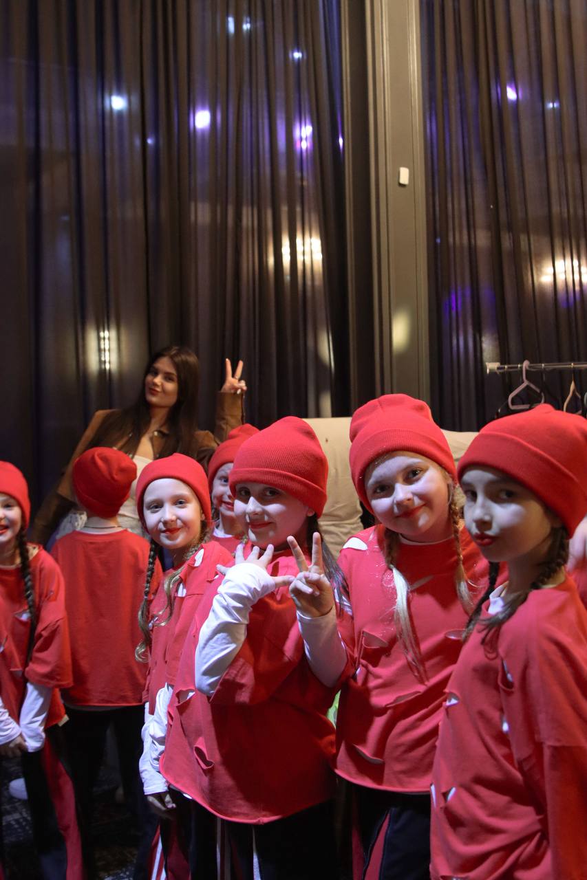 Children in red costumes smiling on stage after a performance