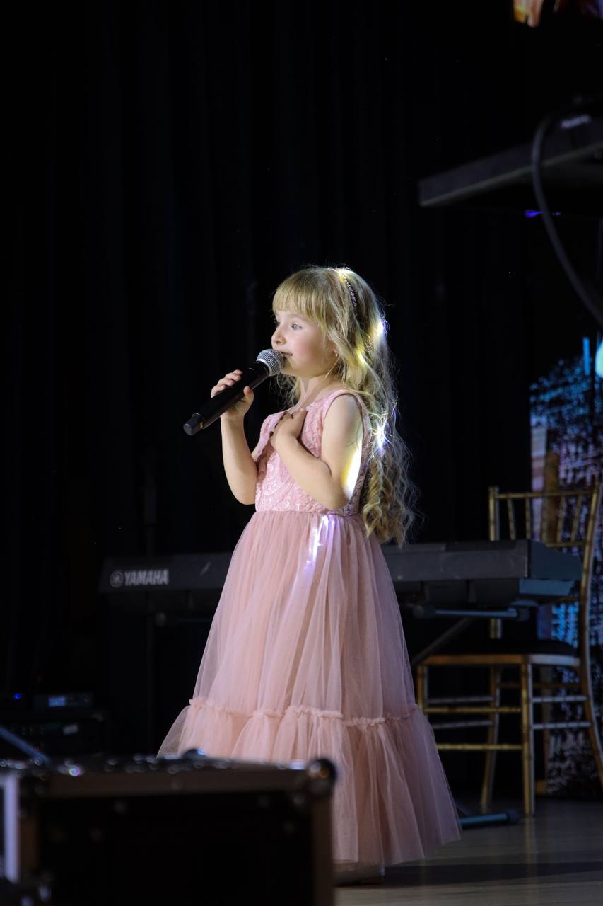 A young singer in a pink dress performing with a microphone