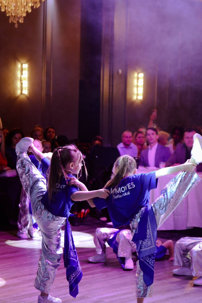 A dance group in matching outfits performing under purple stage light